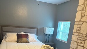 Une chambre à coucher avec un lit, une table de chevet, une lampe, une fenêtre et un mur en pierre.