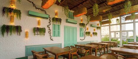 A restaurant with wooden tables and chairs, hanging plants, and green shutters.