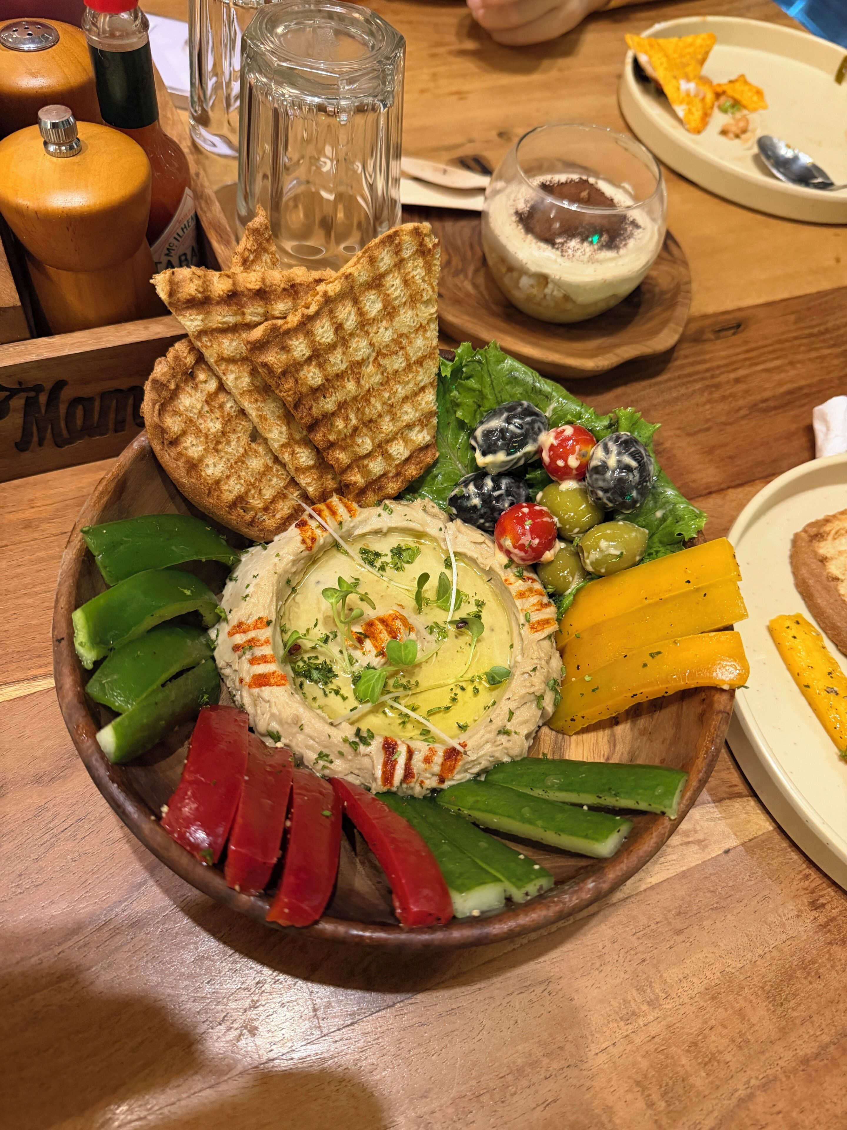 A wooden table with a charcuterie board, a glass of dessert, and condiments.