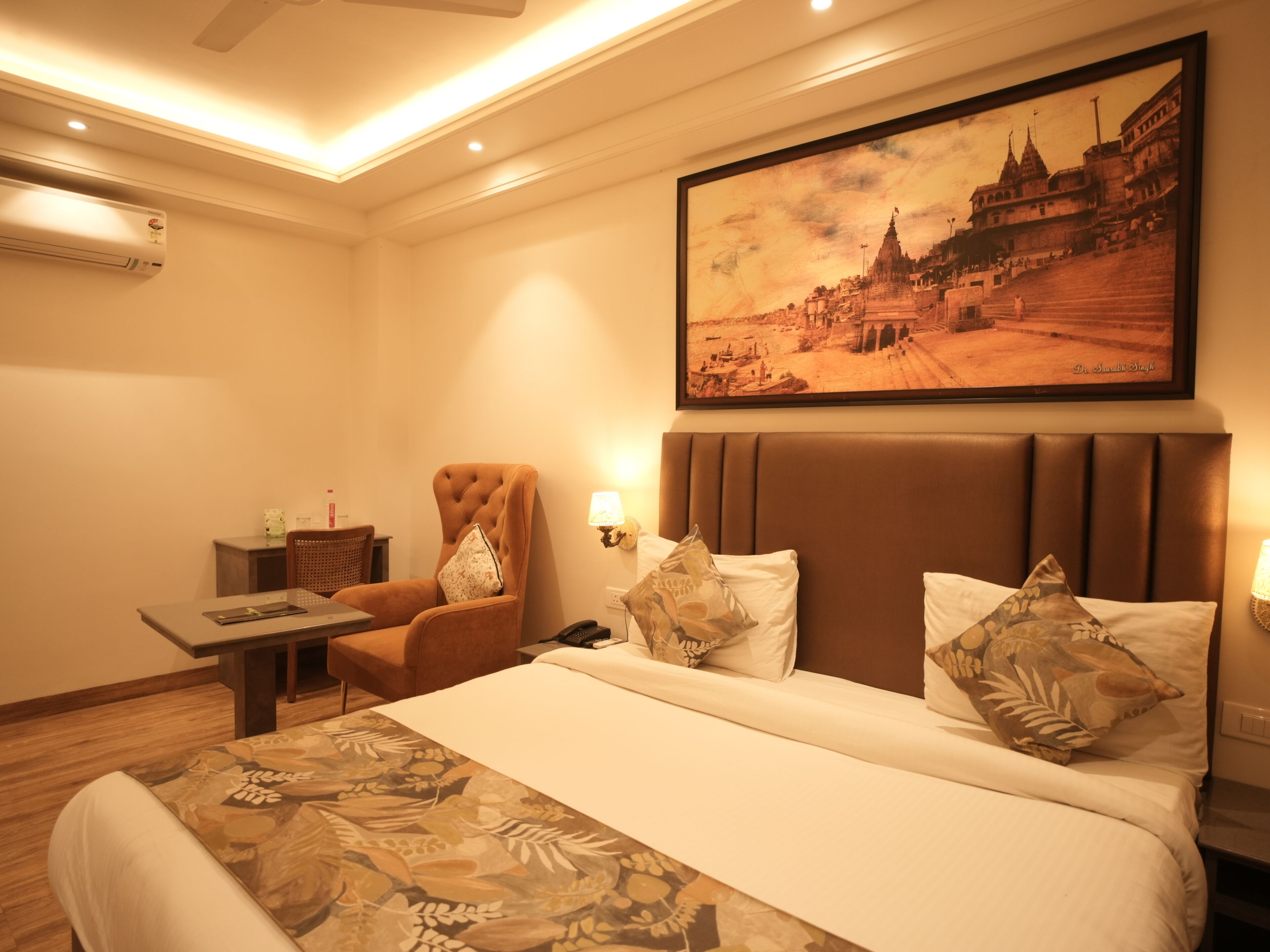 A hotel room with a bed, a chair, a desk, a lamp, and a framed picture on the wall.
