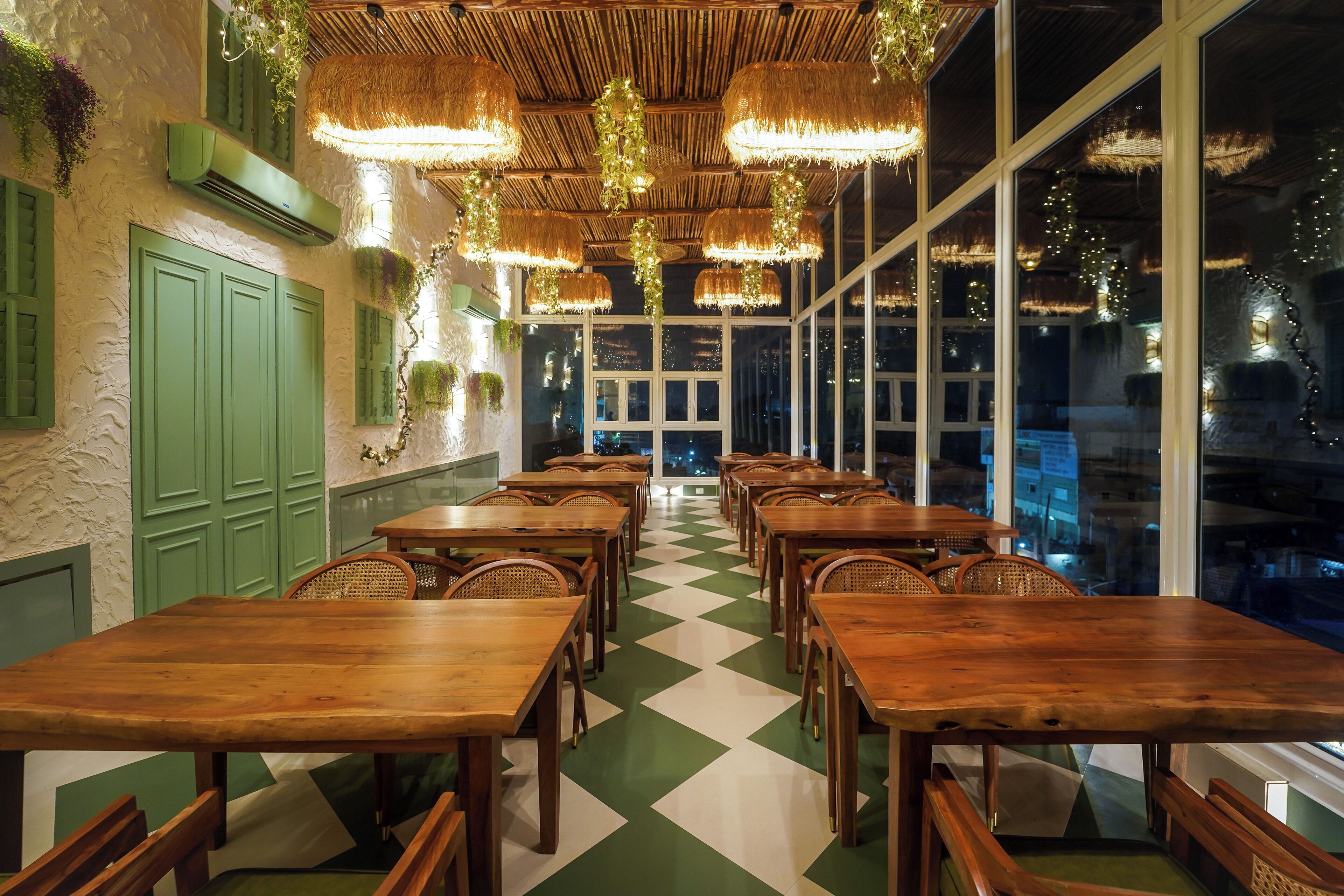 Een restaurant met houten tafels en stoelen, groene muren en grote ramen.