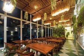 Un restaurante con mesas y sillas de madera, luces colgantes y amplios ventanales.