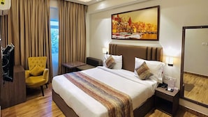 A hotel room with a large bed, a chair, a desk, and a painting on the wall. - Sugar Stars Inn (Varanasi)
