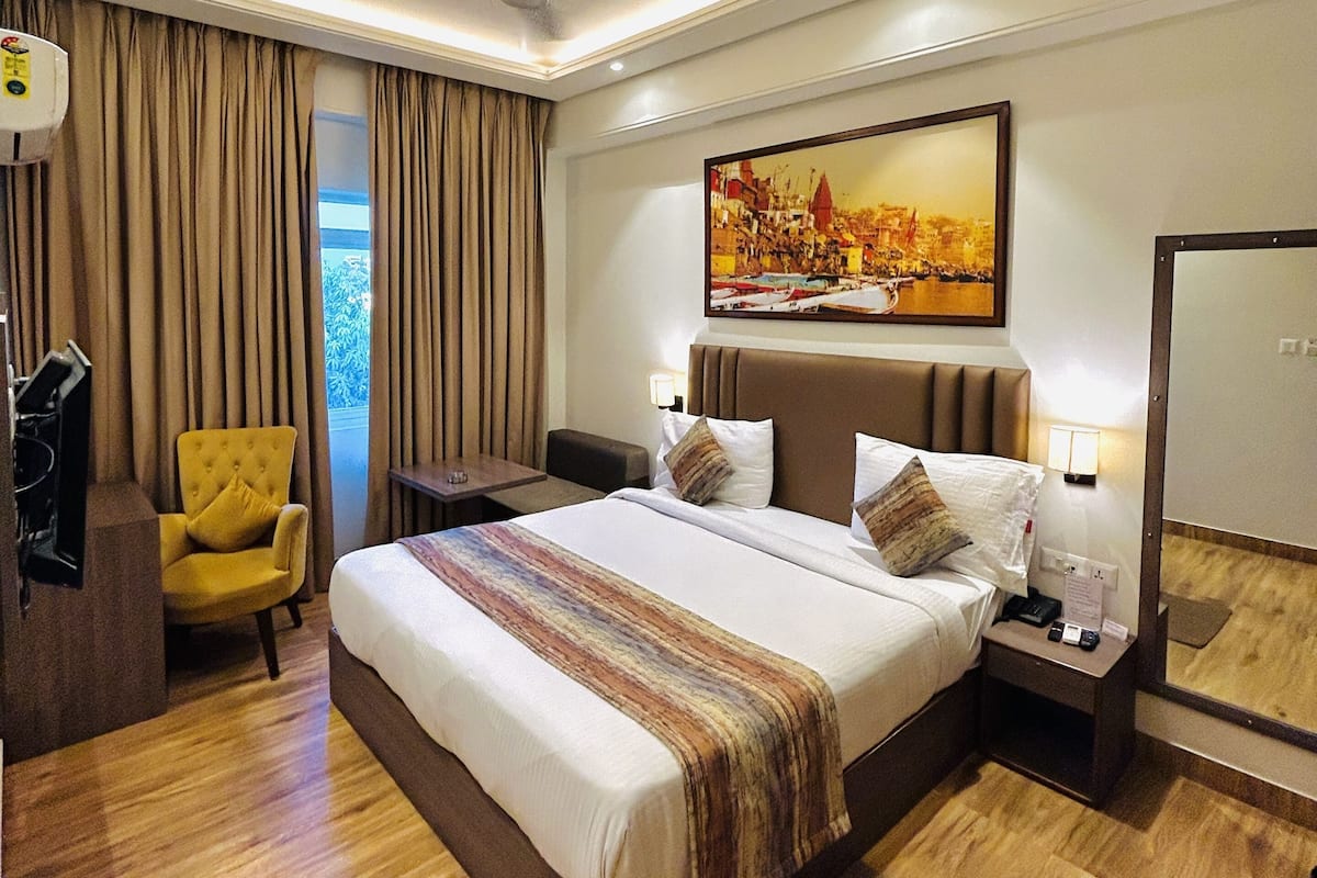 A hotel room with a large bed, a chair, a desk, and a painting on the wall.