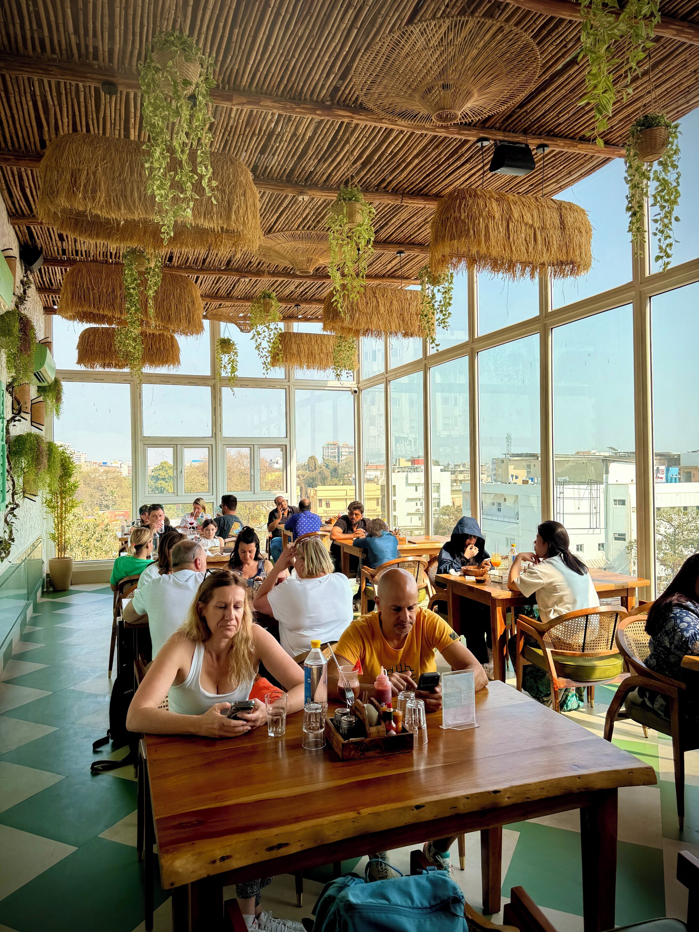 Un restaurant doté de grandes fenêtres, de plantes suspendues et d’un plafond en chaume.
