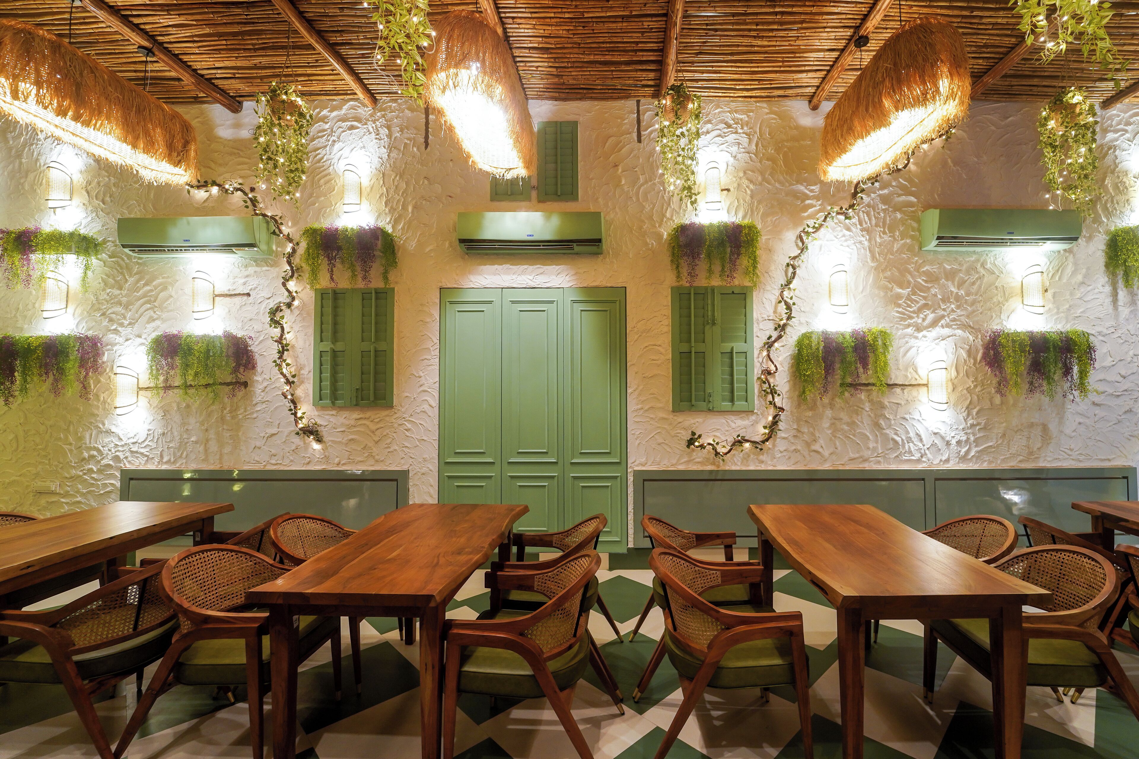 A restaurant with wooden tables and chairs, green shutters, and hanging plants.