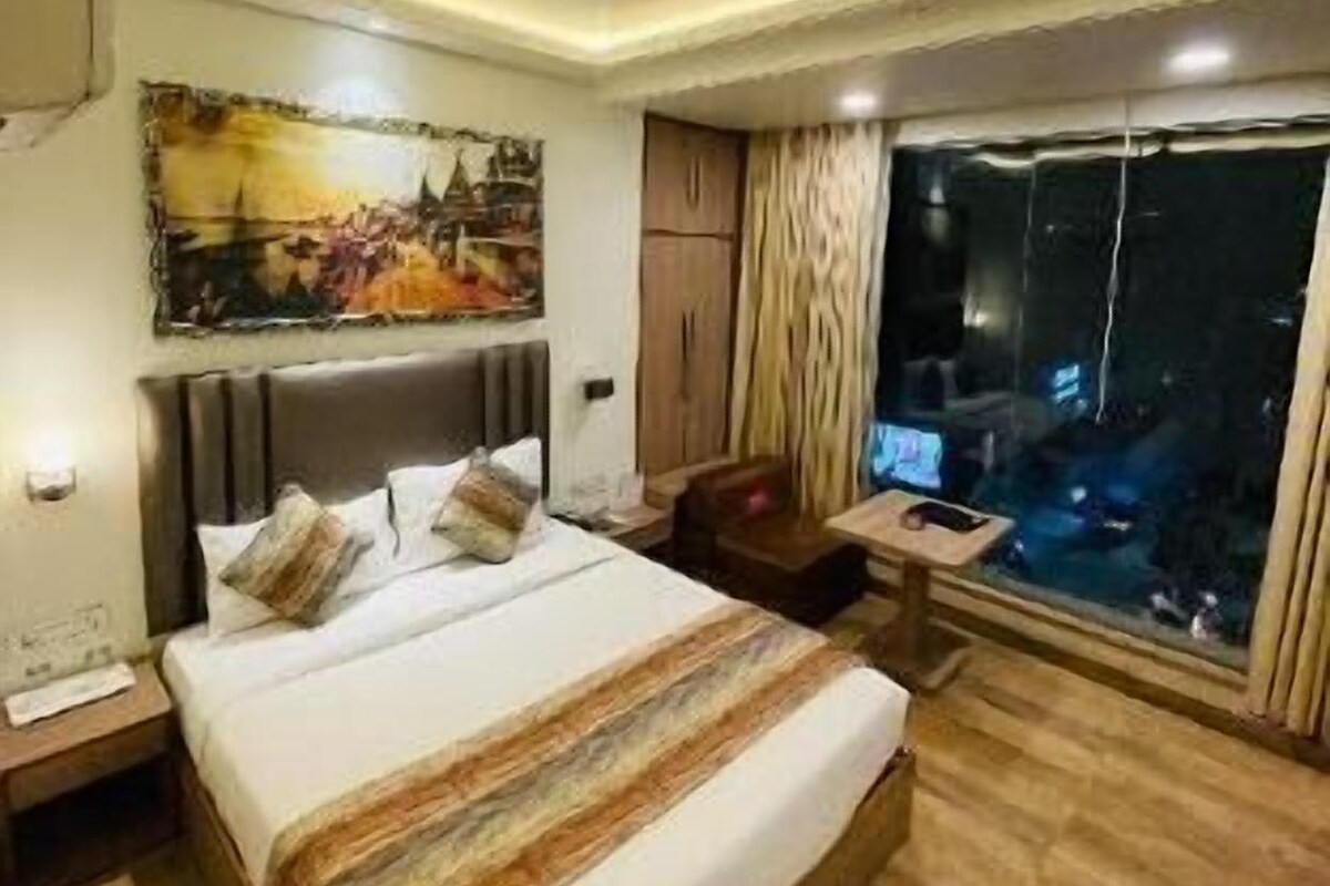 Una habitació d'hotel amb un llit gran, un escriptori amb un ordinador, una finestra amb vista nocturna i un quadre a la paret.