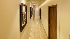 A hallway with a polished marble floor, framed artwork on the walls, and a wooden door with a number plate. - Sugar Stars Inn (Varanasi)