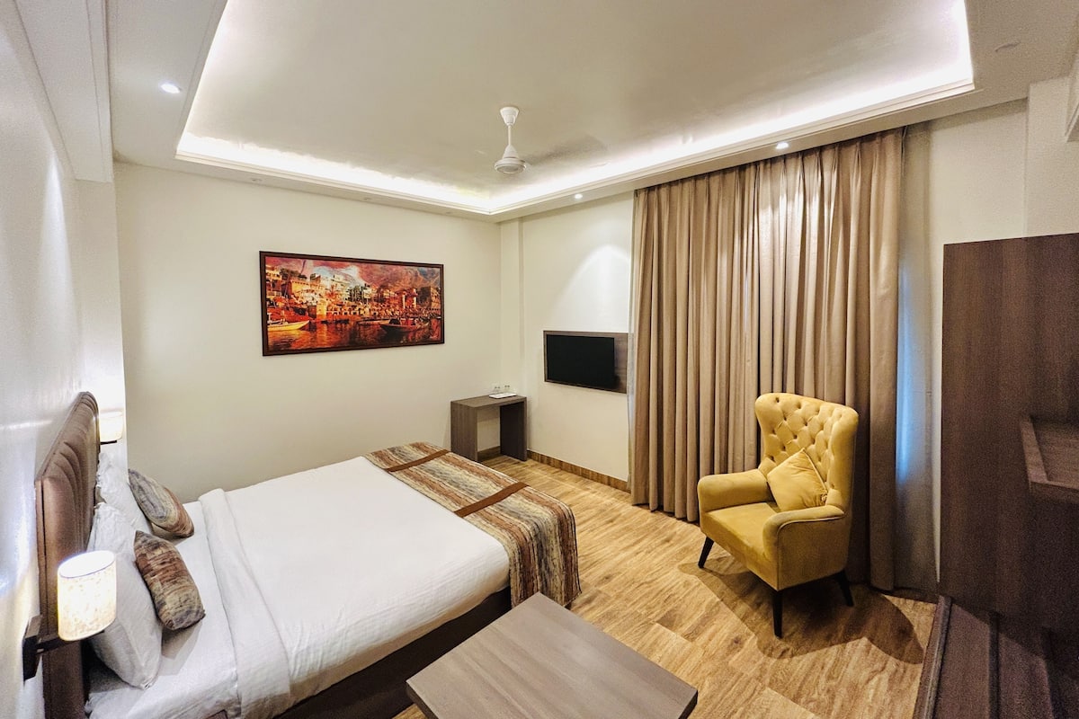 A hotel room with a bed, a sofa, a TV, and a painting on the wall.