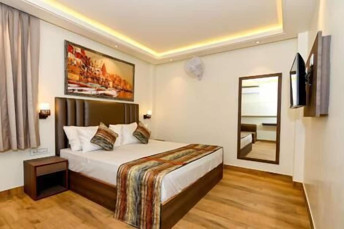 A hotel room with a bed, a nightstand, a painting, a mirror, and a television.