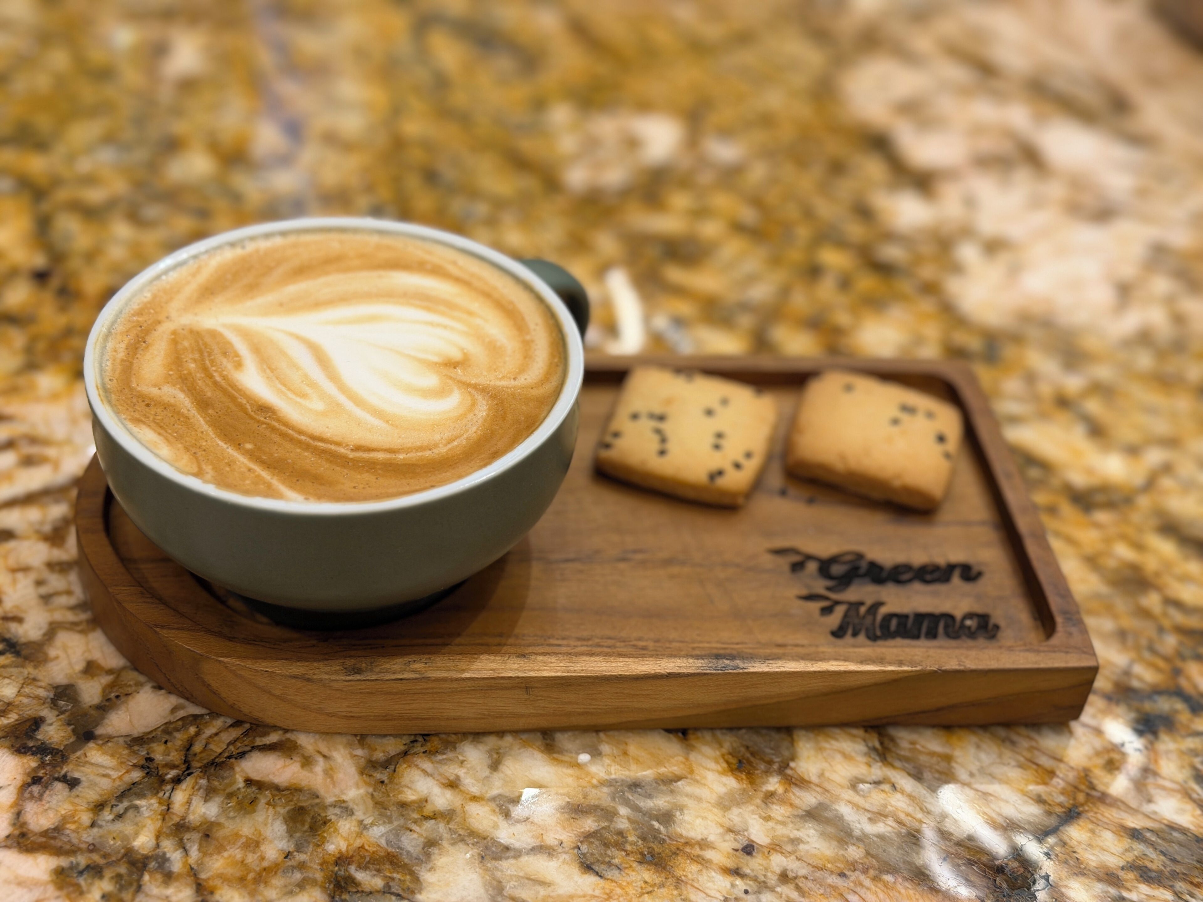 Eine Kaffeetasse mit Latte-Art auf einem Holztablett, zusammen mit zwei Keksen und einem Namensschild.