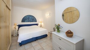 A bedroom with a bed, bedside tables, a dresser, a mirror, and a wall-mounted light fixture.