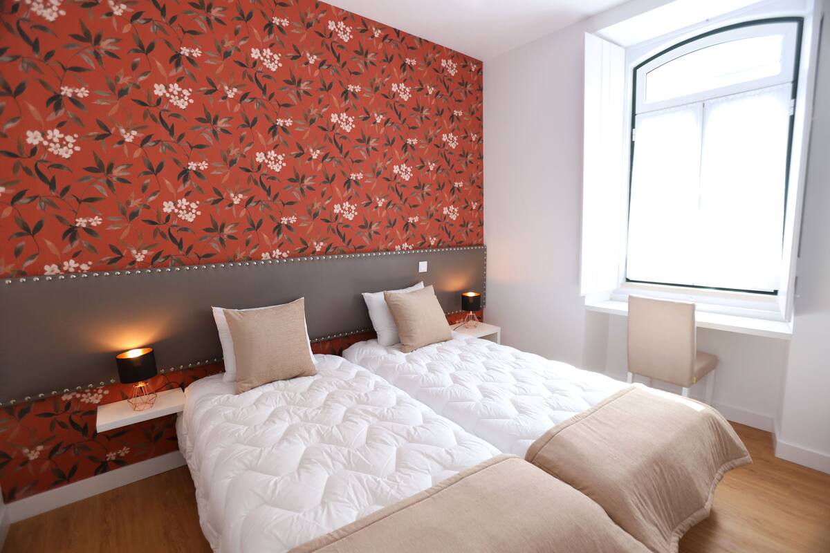 Habitación de hotel con dos camas, una ventana y un estampado floral en el papel tapiz.