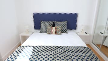 A neatly made bed with a patterned bedspread, a blue headboard, and a bedside table with a lamp.