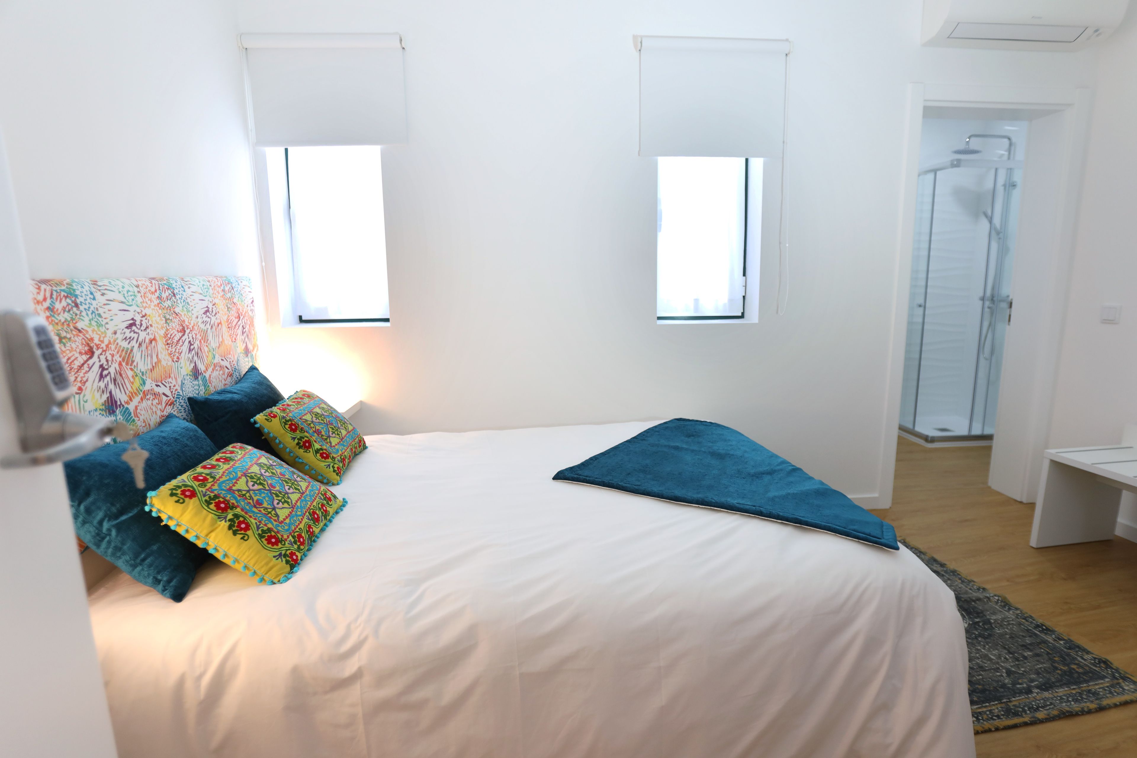 Un dormitorio con cama, almohadas, una mesita de noche, una ventana y una zona de ducha.