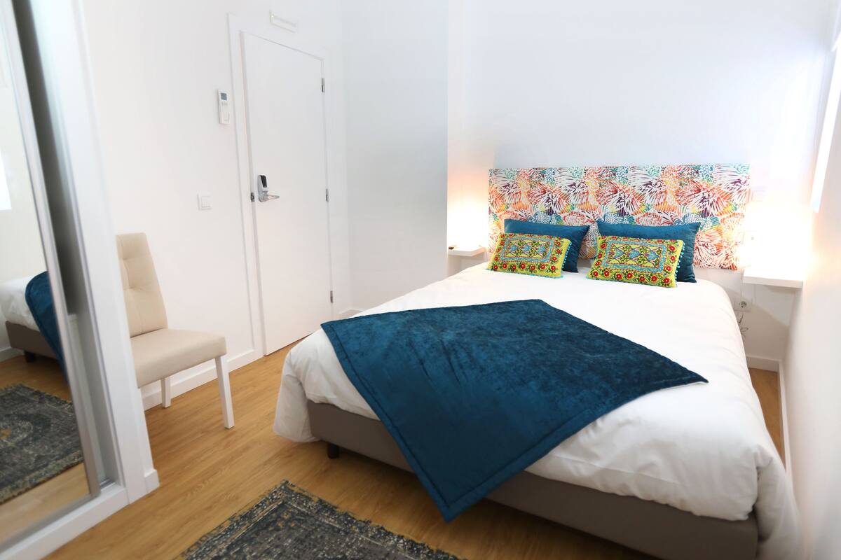 Un dormitorio con una cama, una silla, una puerta y una pared con un diseño colorido.
