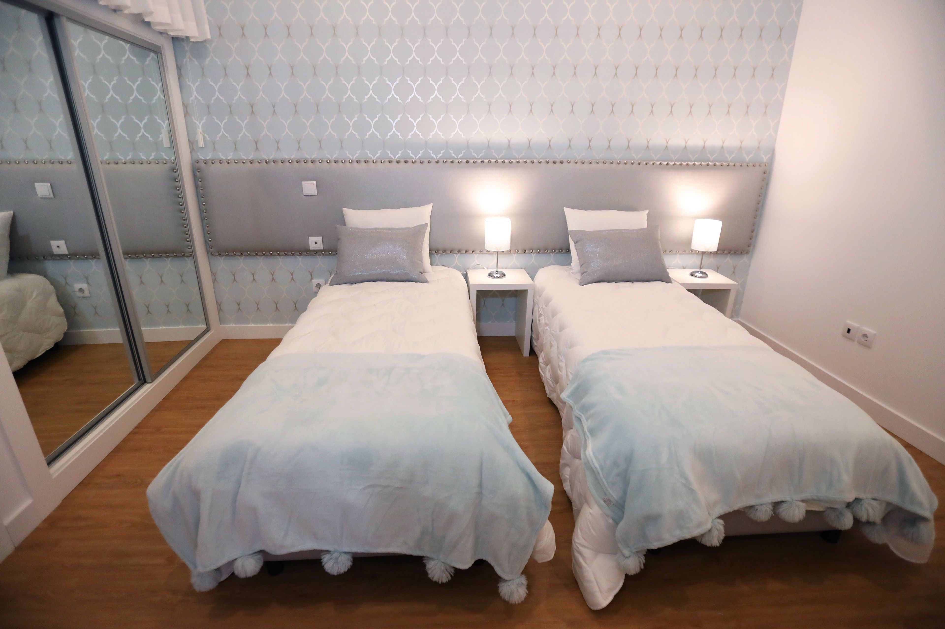 A twin room with two beds, bedside tables with lamps, a large mirror, and a patterned wall.