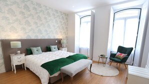 Een slaapkamer met een groot bed, twee nachtkastjes, een bankje, een stoel en een kleine tafel.