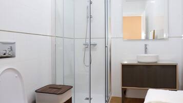 A modern bathroom with a glass shower enclosure, a white toilet, a wooden vanity with a sink, and a mirror above the vanity.