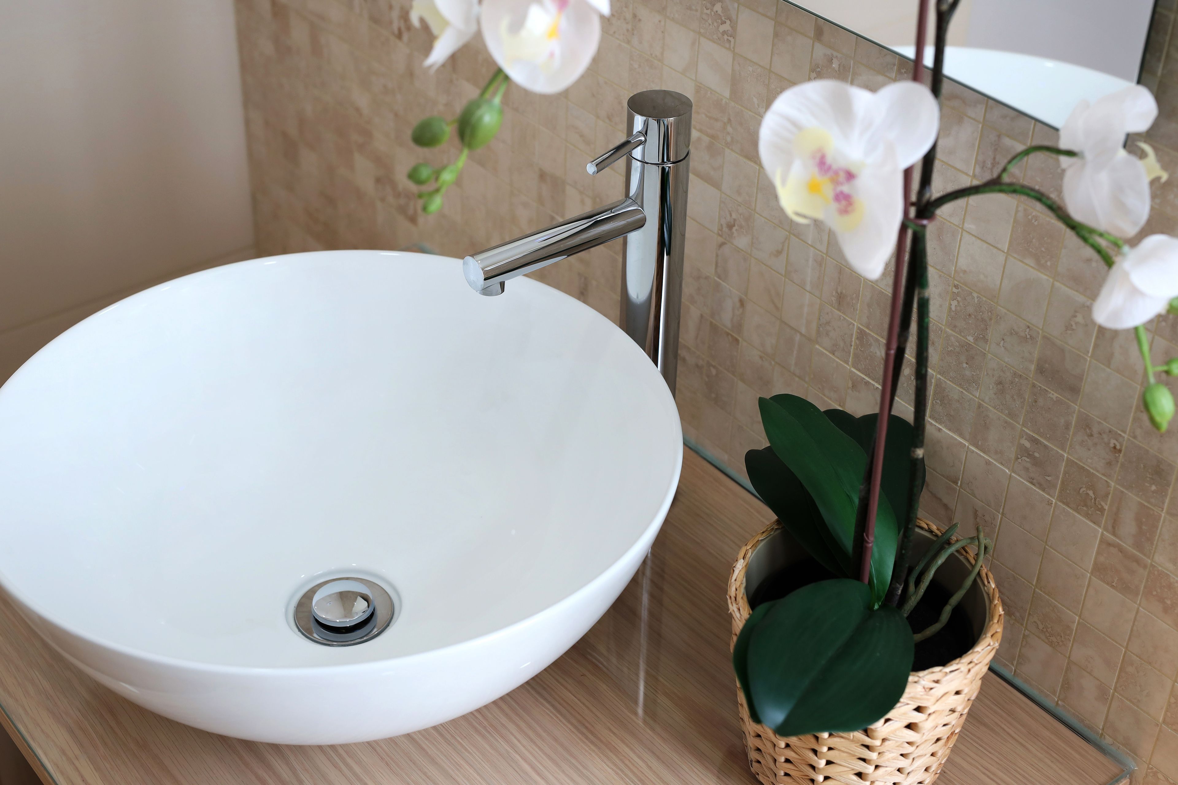 Bany amb un lavabo blanc, un aireix cromat i una orquídia en test.