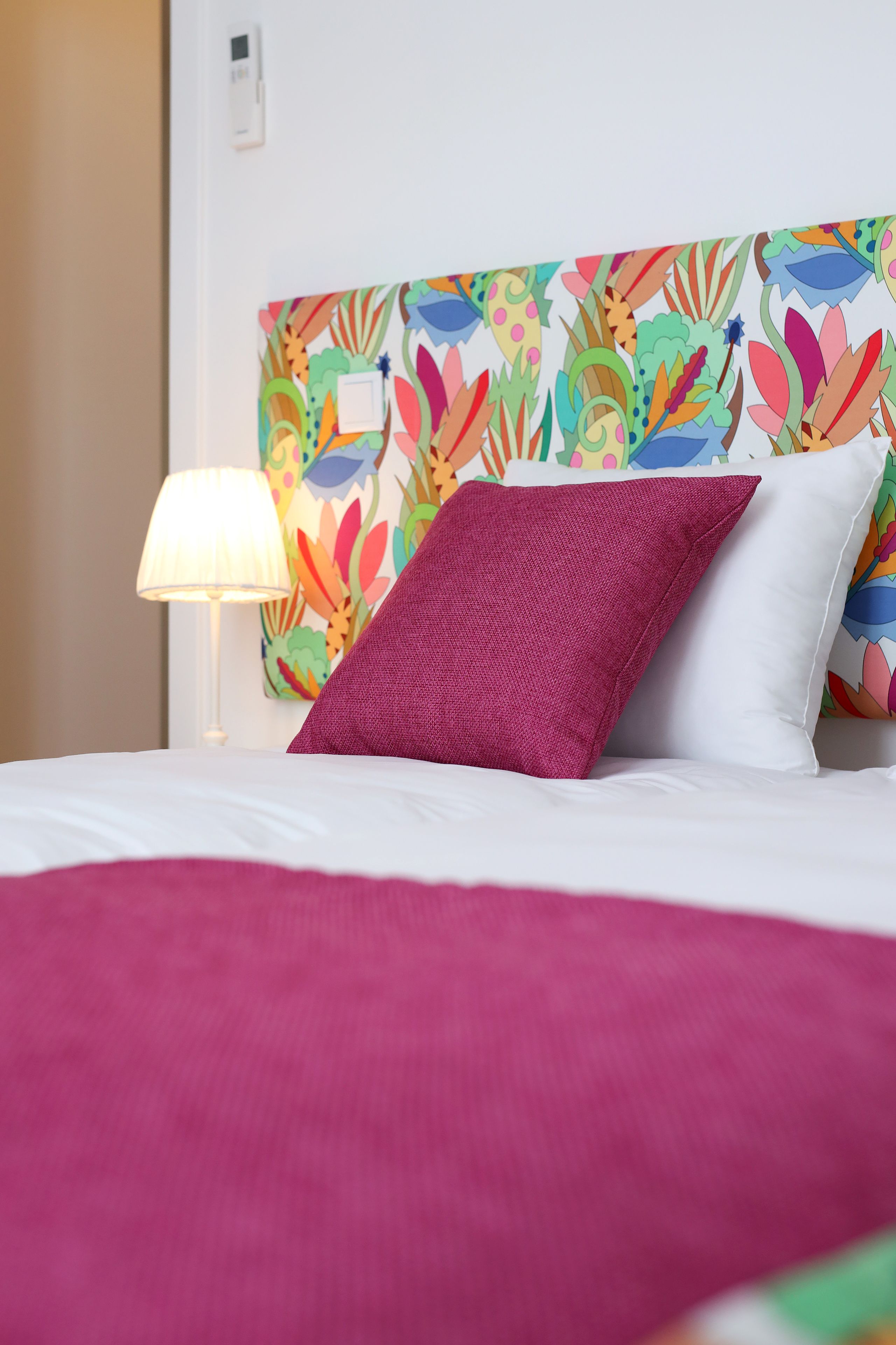 A bed with a colorful headboard, white pillows, and a red blanket.