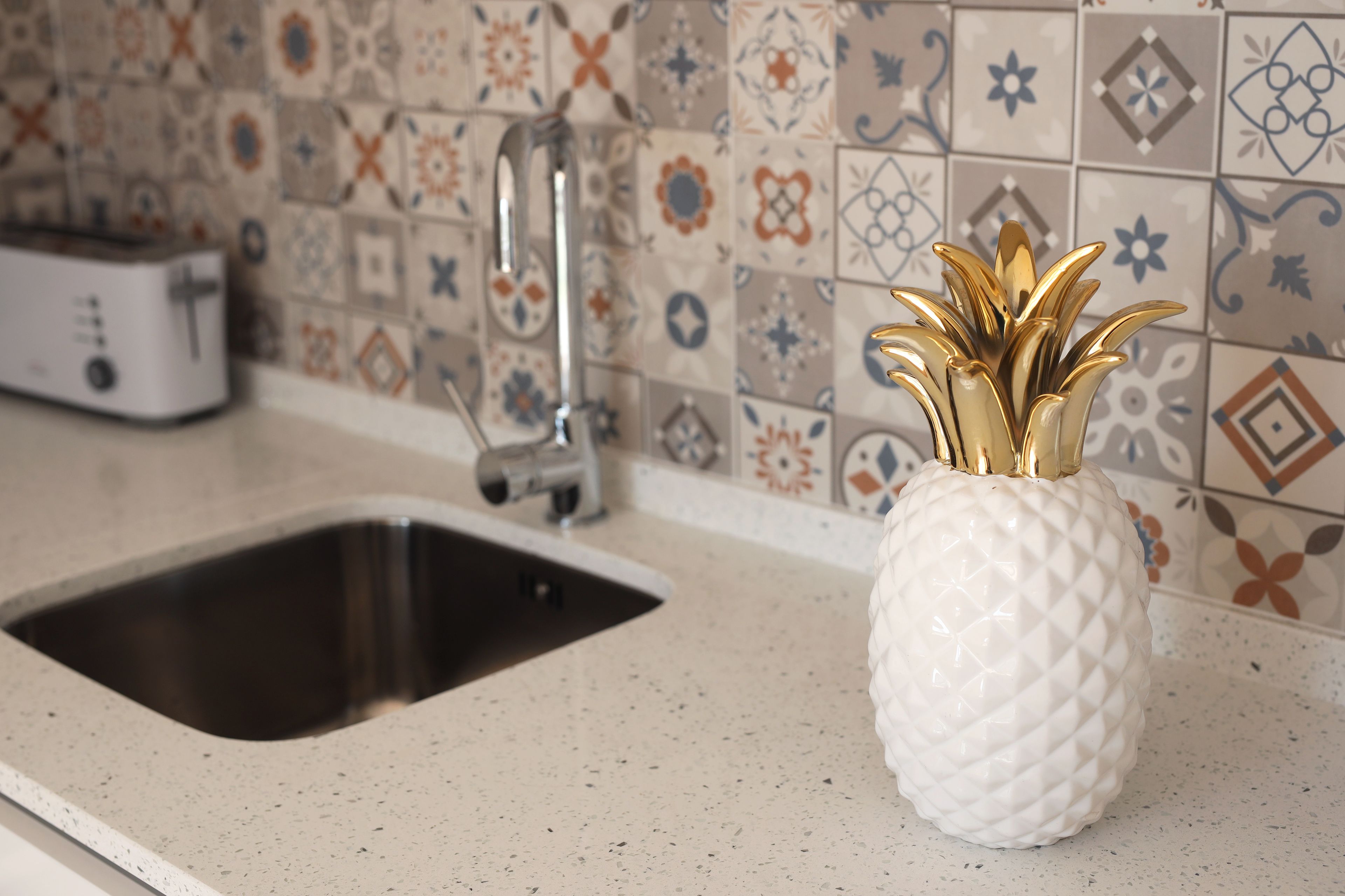 A kitchen with a sink, a toaster, and a decorative pineapple-shaped vase on the counter.