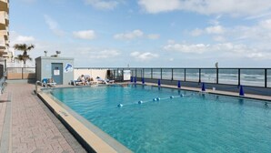 A swimming pool with a view of the ocean, a small lifeguard station, and lounge chairs along the poolside.