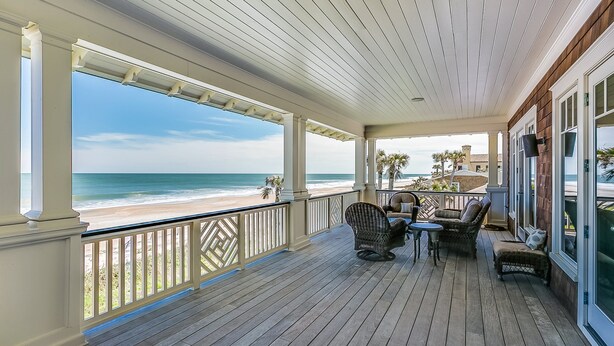 Un espacio al aire libre cubierto con vistas a la playa, que cuenta con suelo de madera, muebles de mimbre y barandilla.