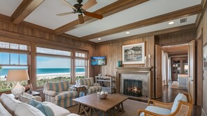 Un salón amplio con chimenea, asientos cómodos y un gran ventanal con vistas a la playa.