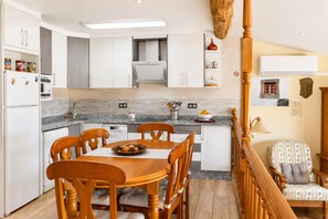 A modern kitchen with white cabinets, a granite countertop, and a dining area with wooden chairs and a table. - Panoramic Terrace, Sunsets, Nature and Stargazing in the Sierra de Béjar (Navalmoral)