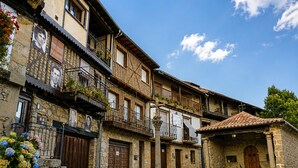 A traditional stone building with a wooden door, a balcony with plants, and a cobblestone street. - Panoramic Terrace, Sunsets, Nature and Stargazing in the Sierra de Béjar (Navalmoral)