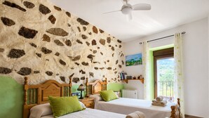 A room with two beds, a ceiling fan, a painting, a radiator, and a view through a window. - Panoramic Terrace, Sunsets, Nature and Stargazing in the Sierra de Béjar (Navalmoral)
