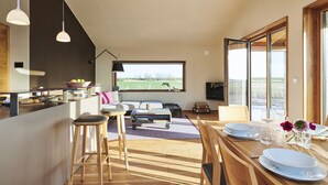 Eine moderne Küche mit einem großen Fenster, Holzboden und einer Essecke mit Tisch für zwei Personen.