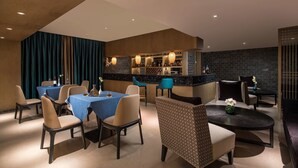 A modern dining area with tables and chairs, a bar area with shelves of bottles, and a patterned chair. - Ramada by Wyndham Zhenjiang City Center (Zhenjiang)