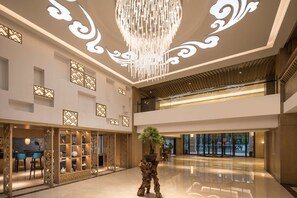A spacious lobby with a modern chandelier, decorative wall panels, and a central potted tree. - Ramada by Wyndham Zhenjiang City Center (Zhenjiang)