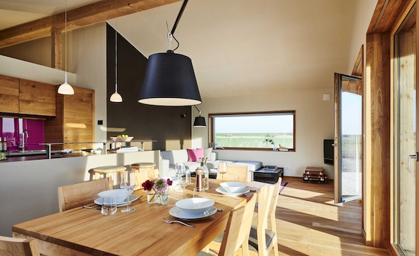 Une cuisine moderne avec des meubles en bois, un coin repas avec une table en bois mise pour le repas, et une grande fenêtre offrant une vue sur l’extérieur.