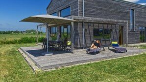 Een modern huis met een houten terras, zitplaatsen buiten en grote ramen.