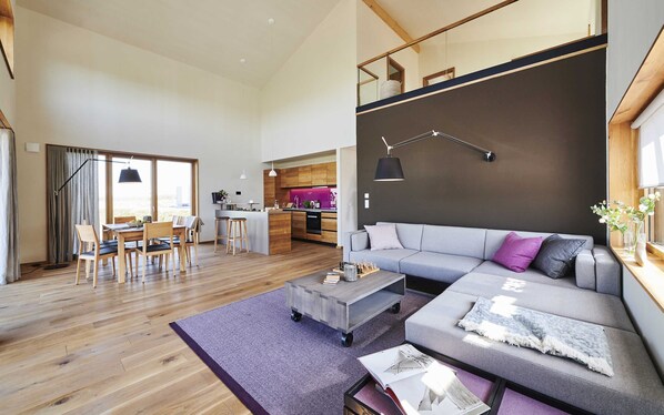 A spacious living area with a modern sofa, a dining table with chairs, and a kitchen in the background.