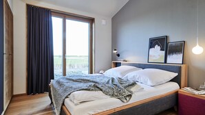 Ein Schlafzimmer mit einem großen Bett, Holzboden, einem Fenster mit Vorhängen und zwei gerahmten Bildern an der Wand.
