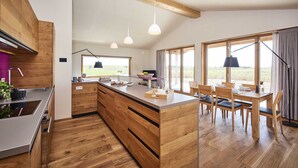 Eine moderne Küche mit Holzschränken, einer zentralen Kochinsel, Pendelleuchten und einem Essbereich mit Tisch und Stühlen.