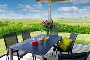 En udendørs terrasse med et bord dækket til to personer, omgivet af stole, og udsigt til et grønt græsareal.