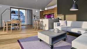 Ein modernes Wohnzimmer mit einem grauen Sofa, einem Holzespeisetisch mit Stühlen, einem Couchtisch auf Rollen und Pendelleuchten.