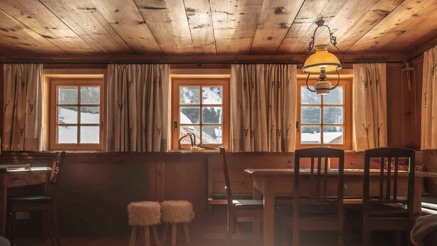 Interior acogedor de una cabaña con paredes de madera, una mesa de comedor, sillas y una alfombra de piel.