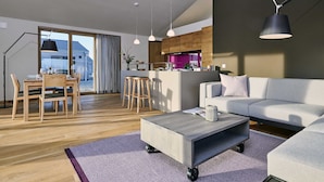 Un salon moderne avec un canapé gris, une table à manger en bois avec des chaises, une table basse à roulettes et des luminaires suspendus.