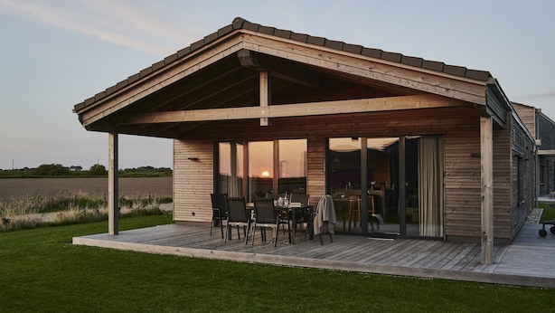 Une maison moderne dotée d’une terrasse en bois, de grandes portes-fenêtres coulissantes et offrant une vue sur le coucher de soleil.