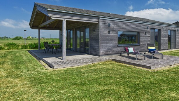 A modern house with a covered patio, outdoor seating, and a view of the surrounding landscape. - (03) Gud Jard Lodge Leo, Cat. FamilyTime - Designer holiday home Leo (03) with (Pellworm)