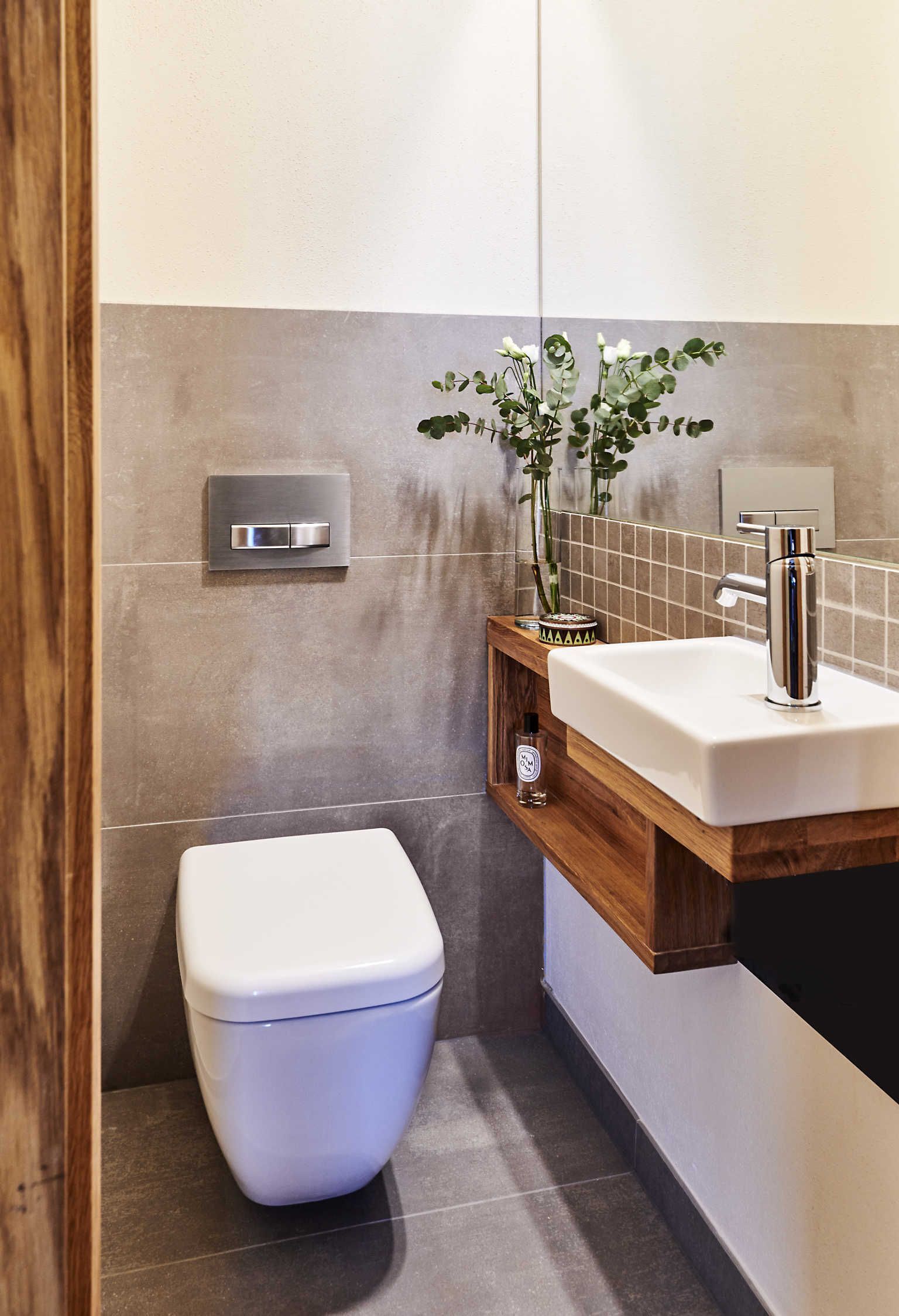A modern bathroom with a white toilet, a wooden vanity with a sink, and a wall-mounted light fixture.