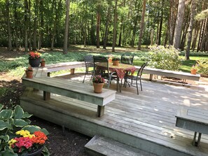 Enjoy a serene meal on the deck surrounded by lush gardens and tall trees.
