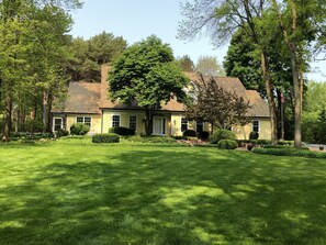 Stunning two-story home with a central entrance and beautiful views of the surrounding lawn and trees.