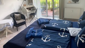 Quarto com cama com roupa de cama temática náutica, escrivaninha com cadeira e vista para o verde lá fora.